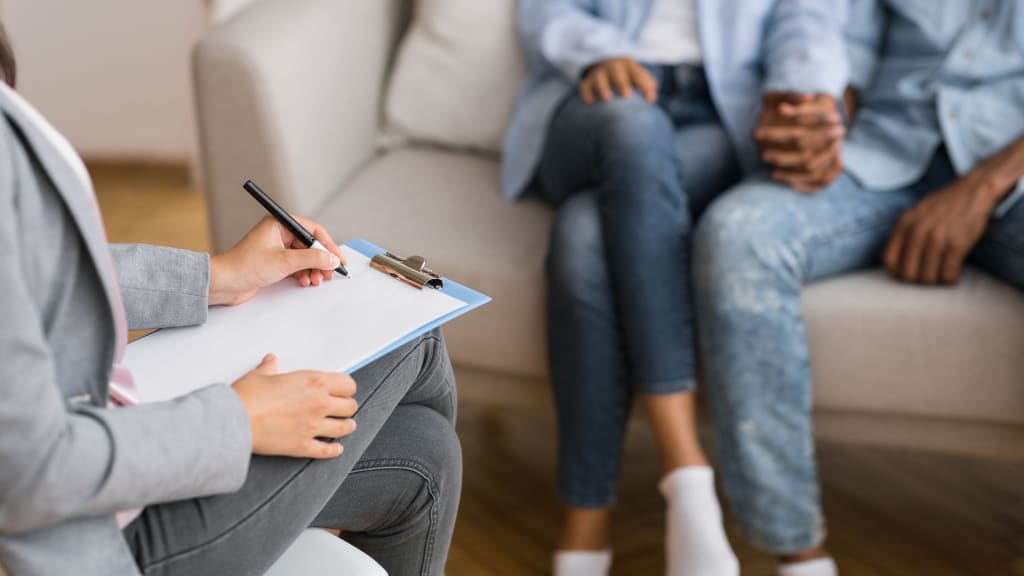 Afro couple holding hands on couch during marriage counseling session